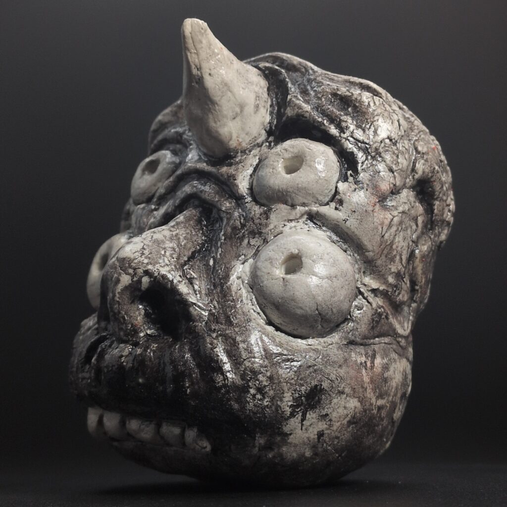 A hand-sculpted clay effigy of a Hōsōshi yokai, featuring a weathered, multi-eyed creature with a prominent horn and distressed monochromatic finish.